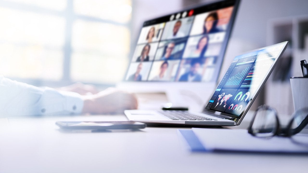 An employee's laptops at work displaying dashboards and a virtual video call.