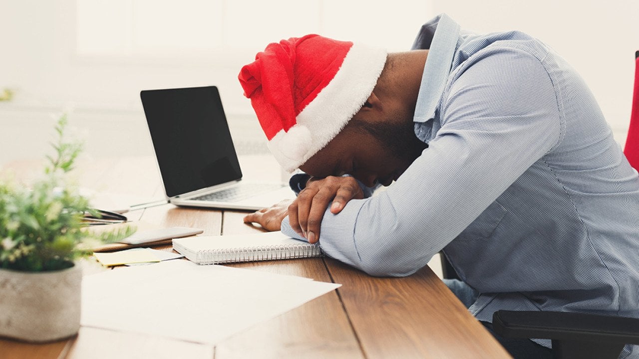 A tired businessman wearing a Christmas hat while asleep at work.