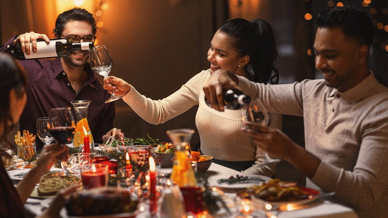 A group of happy friends pouring wine in their glasses during Christmas dinner.