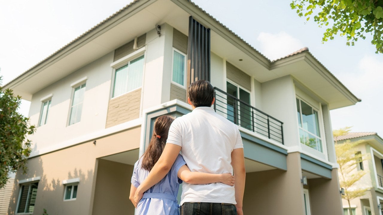 Back portrait of a young couple standing in front of their newly-bought home.