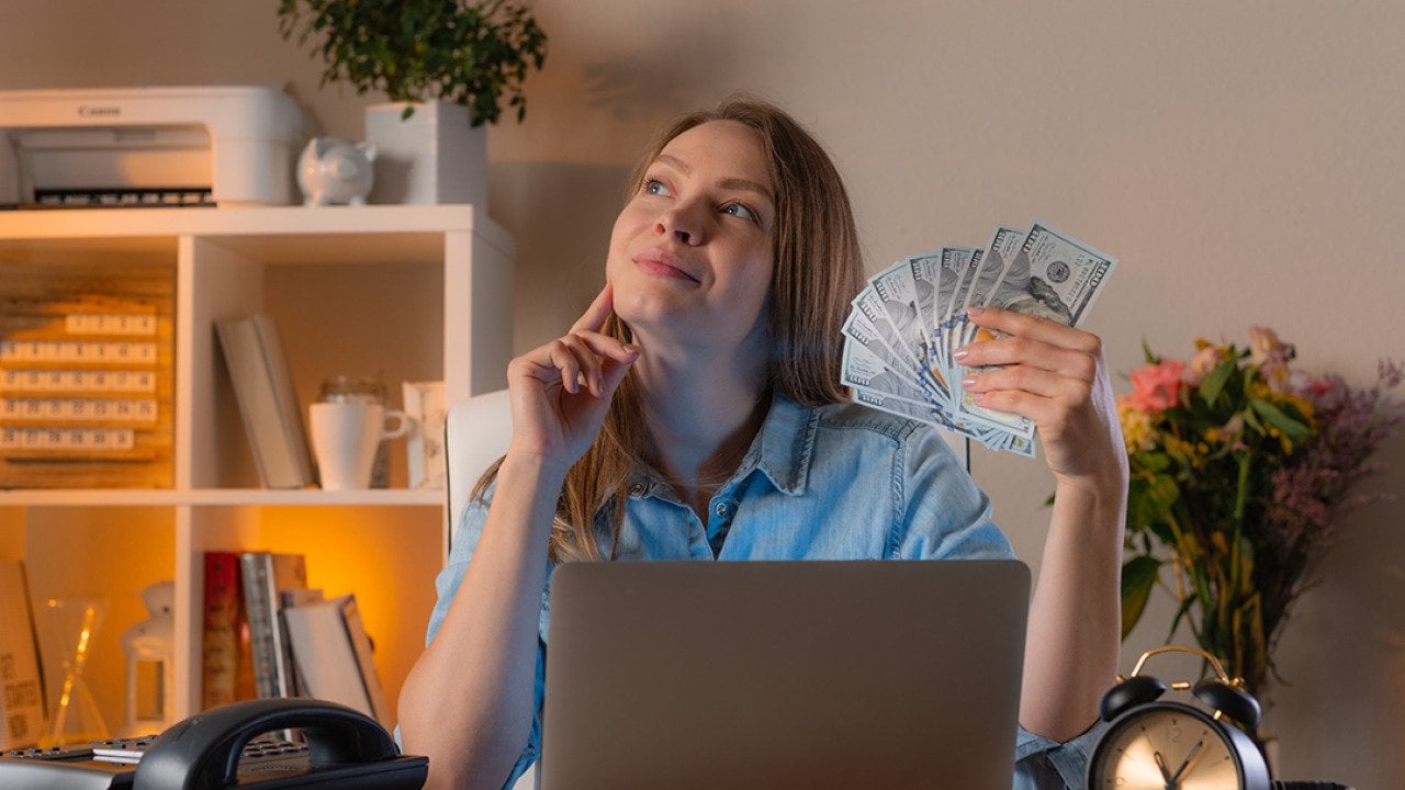 A female manager holding cash daydreaming in an office.