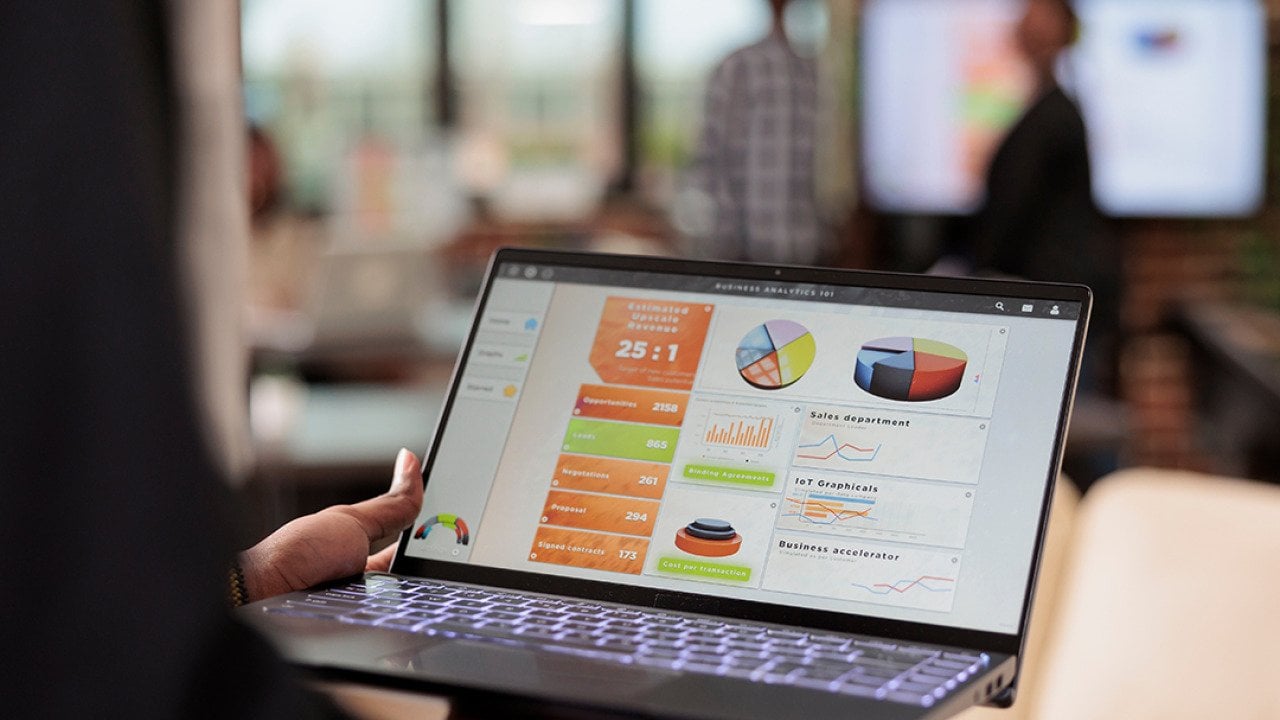 A businessperson holding a laptop that displays data charts and graphs.
