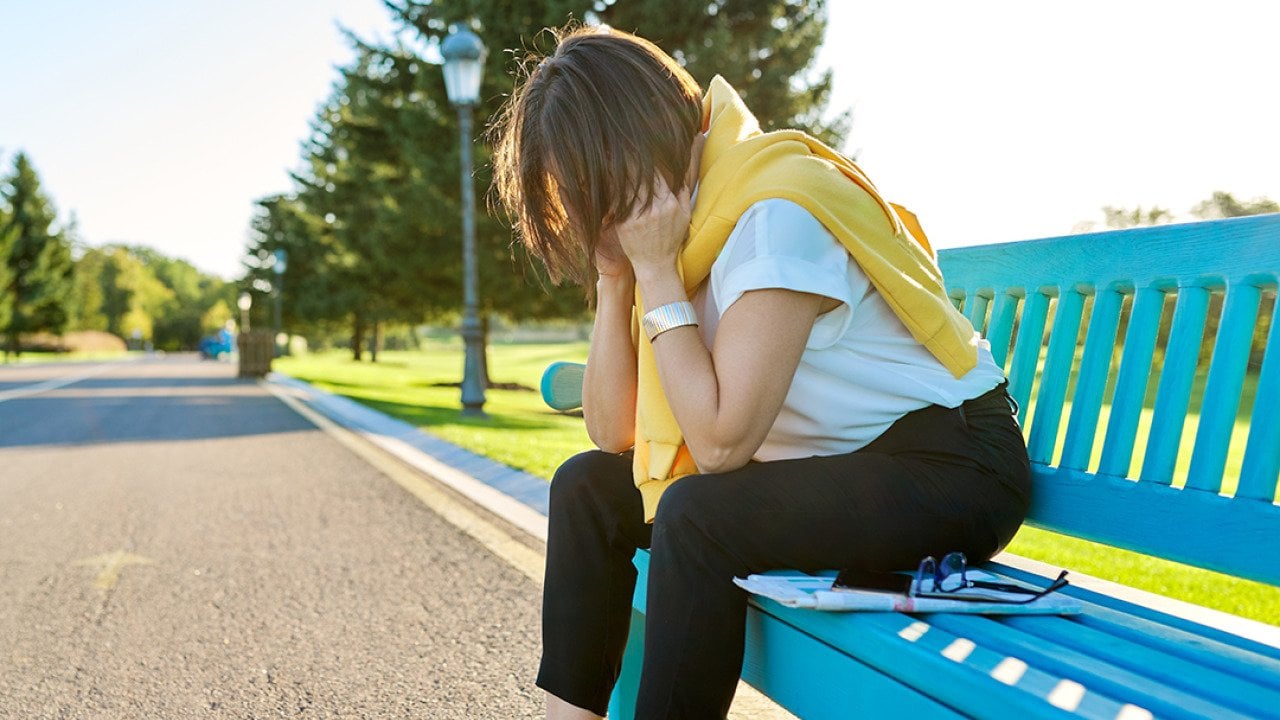 A tired woman sitting on a bench in the park, taking a break from fitness run.