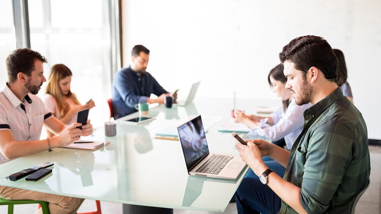 A business team in a meeting room but each member is using their phone.