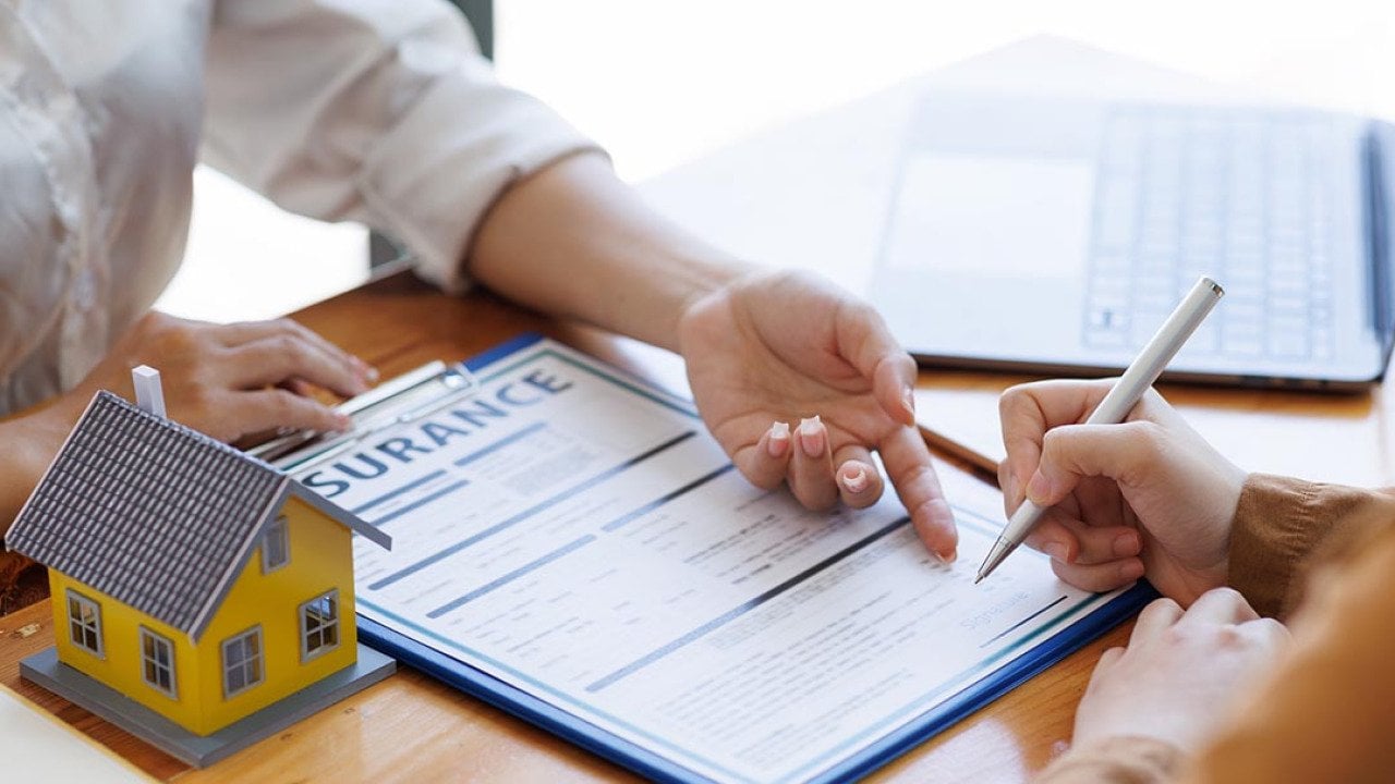 Two people whose faces are not visible review paperwork, representing a real estate broker agent presenting form customer to sign for insurance agreement.