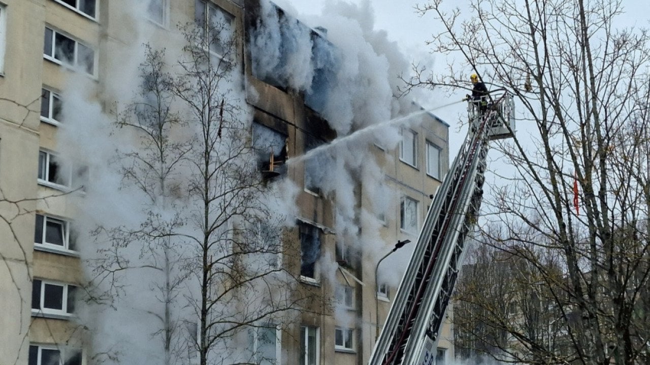 A firefighter on a lift sprays water from a hose into an apartment building as smoke pours out..