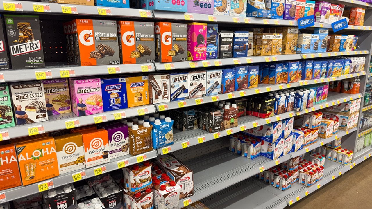 Shelves stocked with protein bars in a grocery store.
