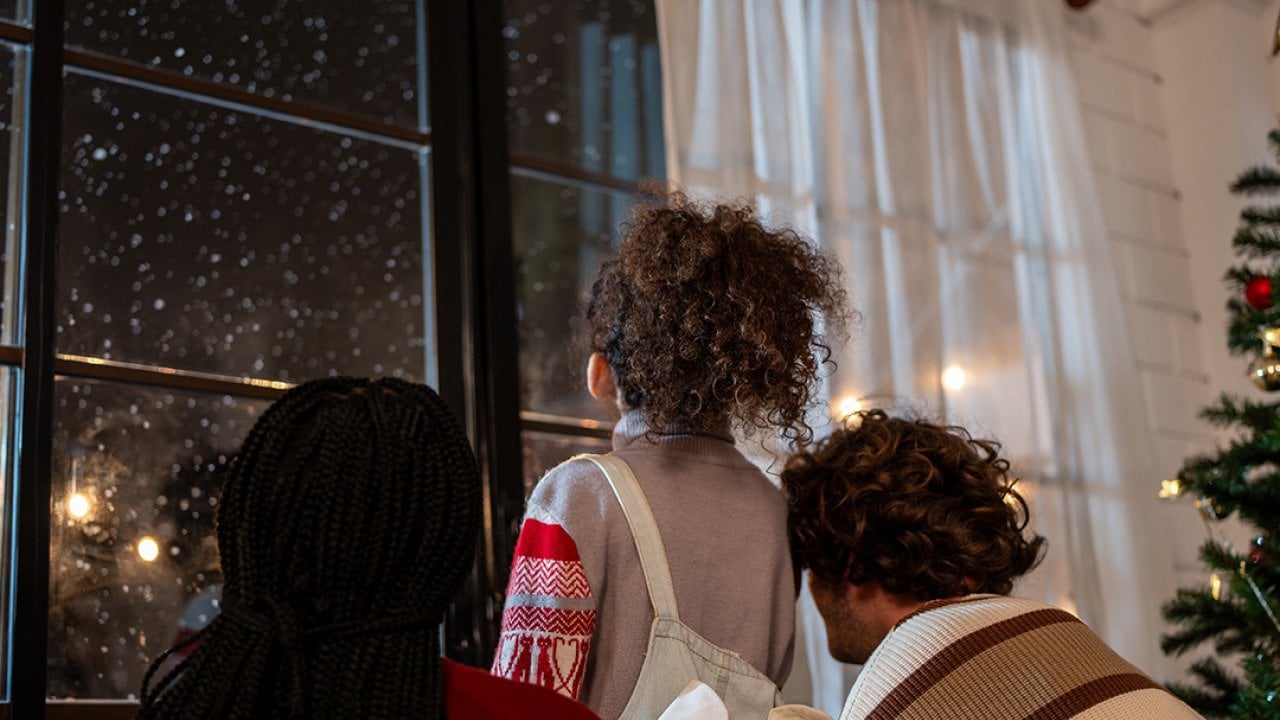 A family looking at the window to see snowfall at night.