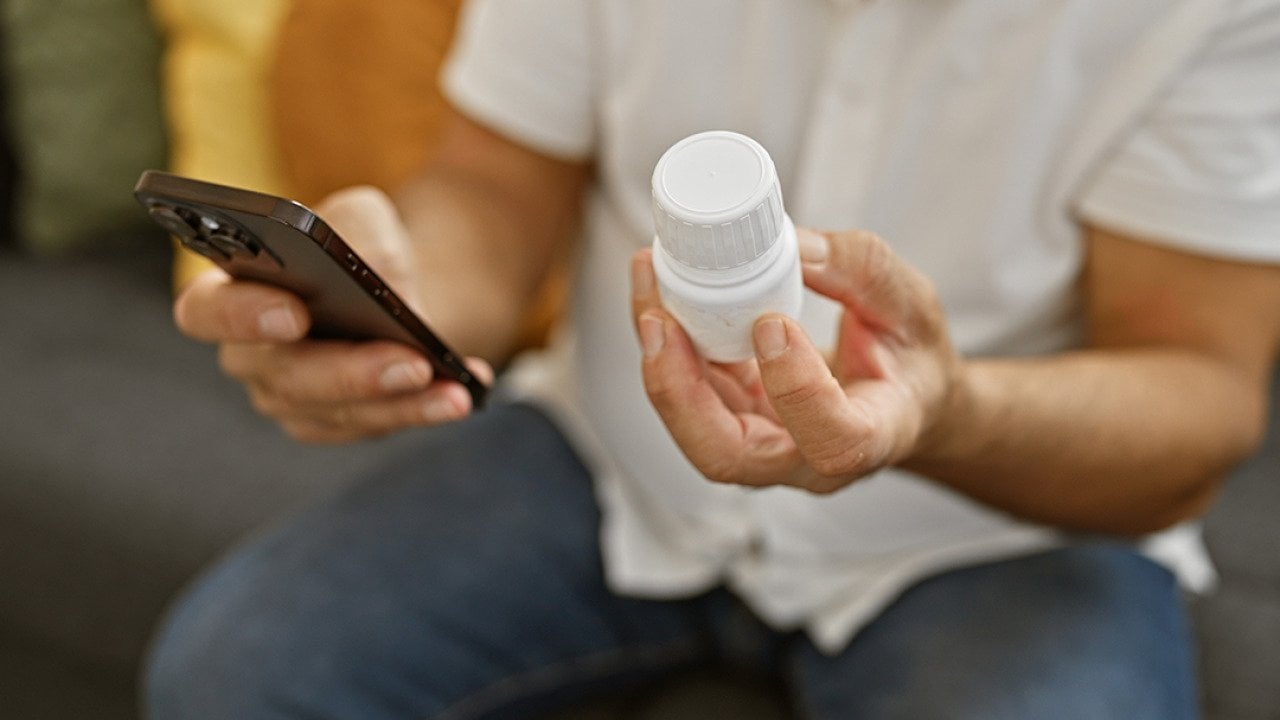 Person holding a prescription medicine bottle and checking info using smartphone.