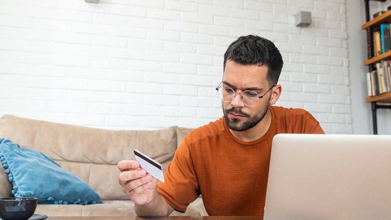 A stressed man reviewing credit card and utility expense documents at home.