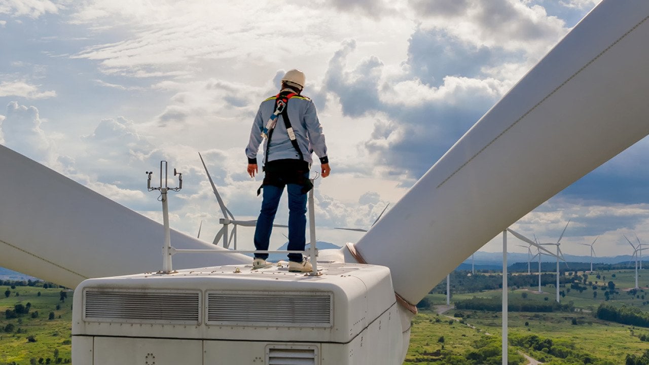 A windmill engineer on top of a wind turbine for inspection.