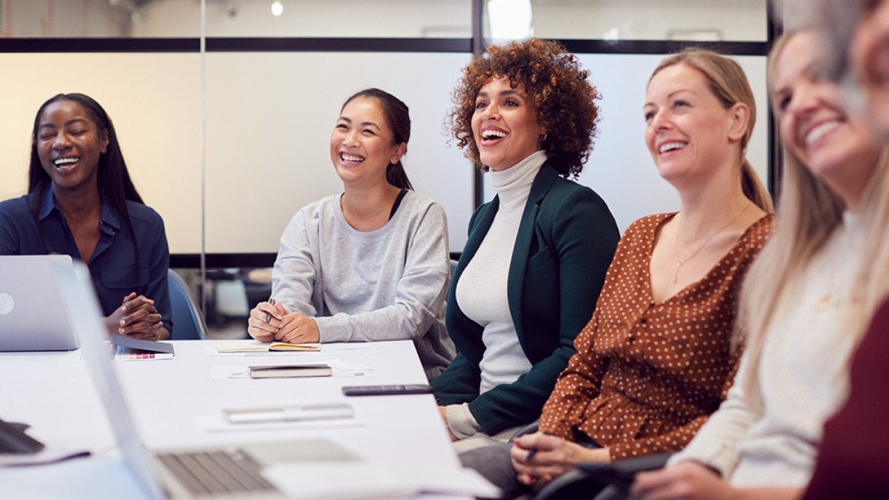A group of business women listening to a presentation in a meeting room.