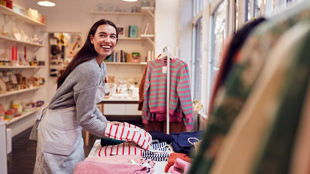 A female business owner arranging stock clothing for her store's window display.