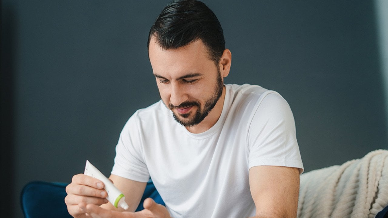 A man squeezing a tube of face cream.