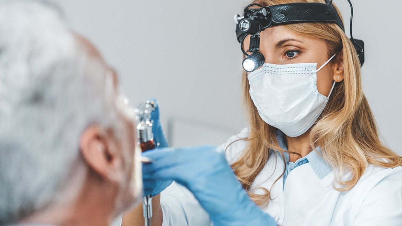 Close up of a female otolaryngologist making an examination of a senior patient's oral cavity.