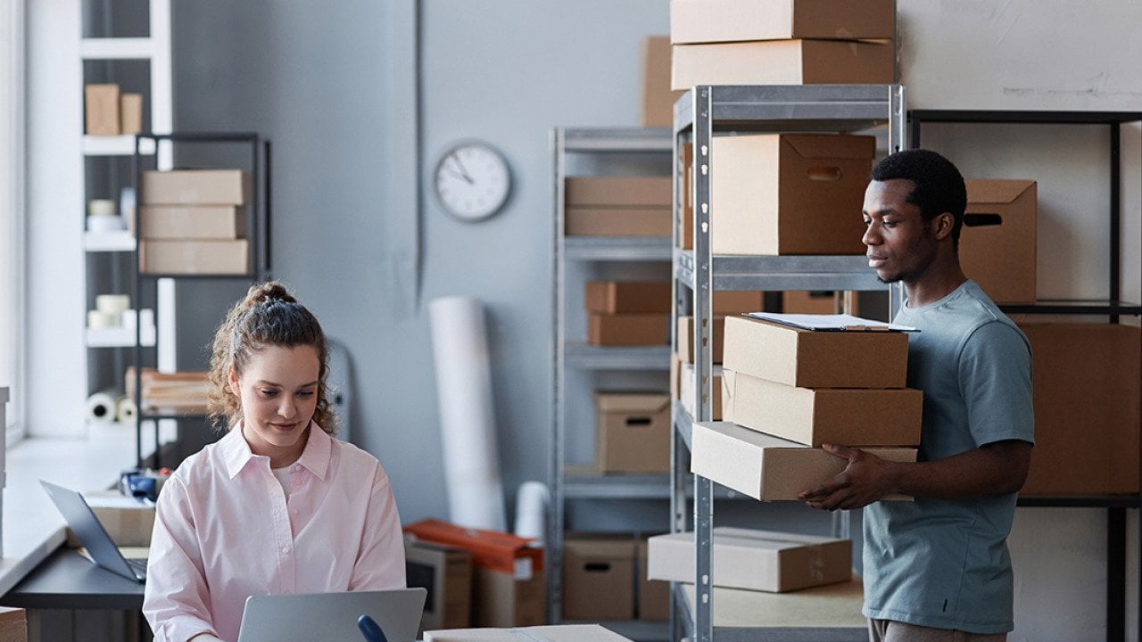 Two members of a small business in a warehouse preparing to send packages.