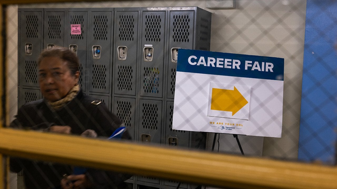 A window view of a jobseeker and a signage with an arrow pointing to where a career fair is situated in New York City.