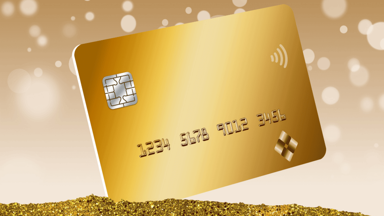 A gold credit card is seen in a pile of gold dust with bokeh circles in the background in a 3D illustration.