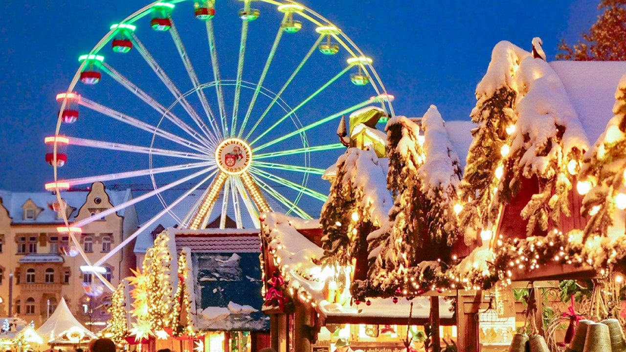 A ferris wheel lights up the night sky during twilight at the Erfurt Christmas Market with vendors selling festive goods in the foreground.