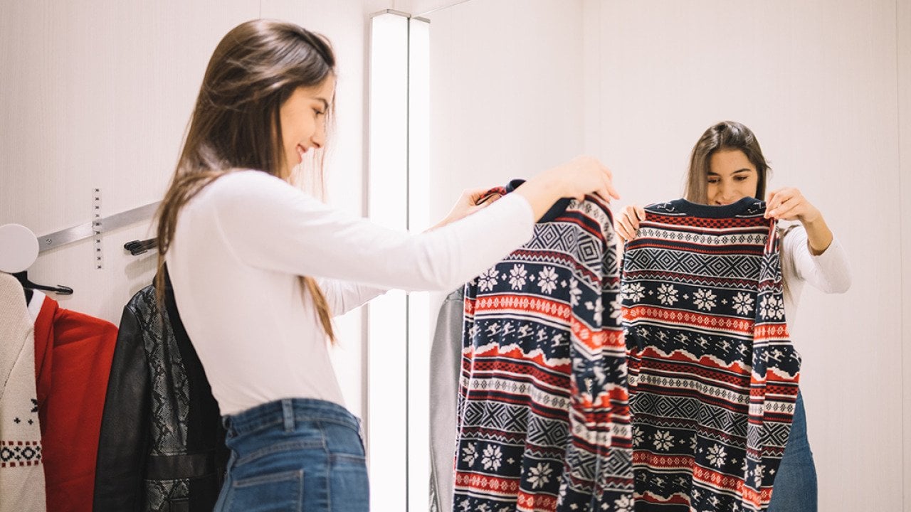 A young woman looking at a winter sweater in a dressing room.