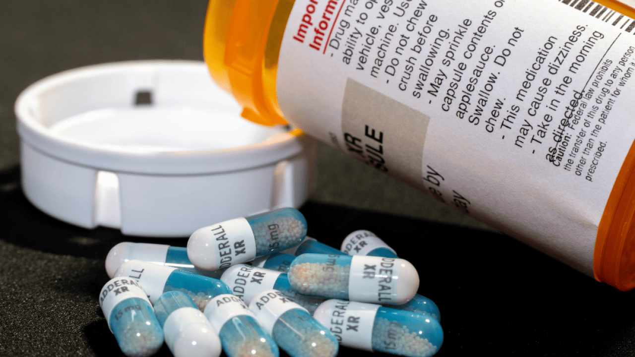 Closeup of an open bottle of adderral medication with some pills laying next to the bottle.