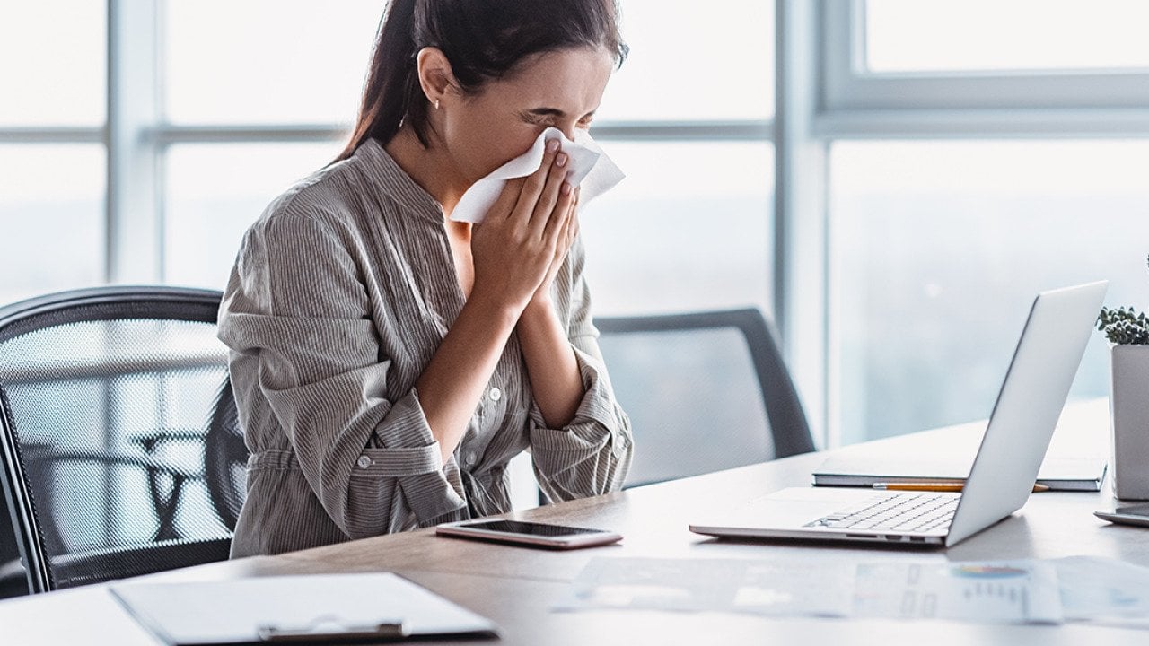 A sick businesswoman blowing her nose at work.