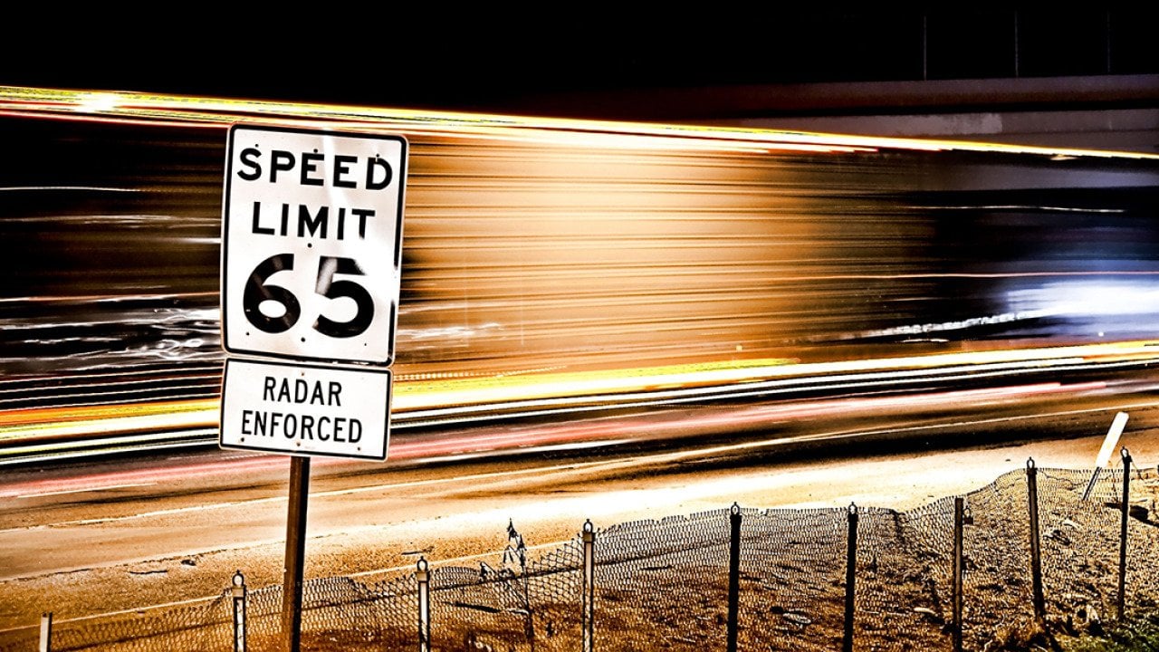 65 mph speed limit sign with a background of long exposure trails.