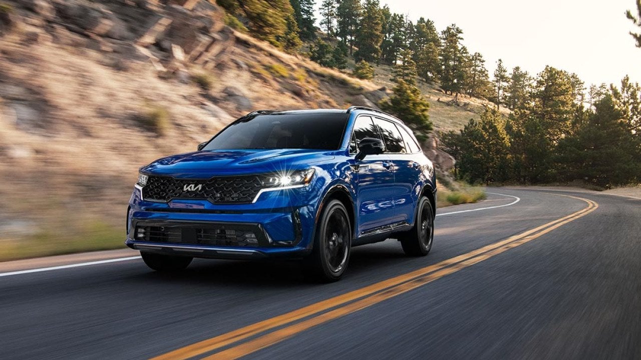 A front 3/4 view of a blue 2023 Sorento SX driving on a mountain road.