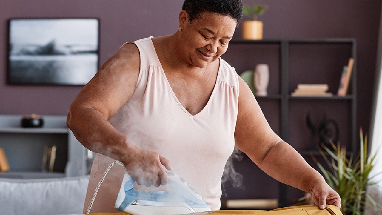 A senior woman happily ironing clothes at home.