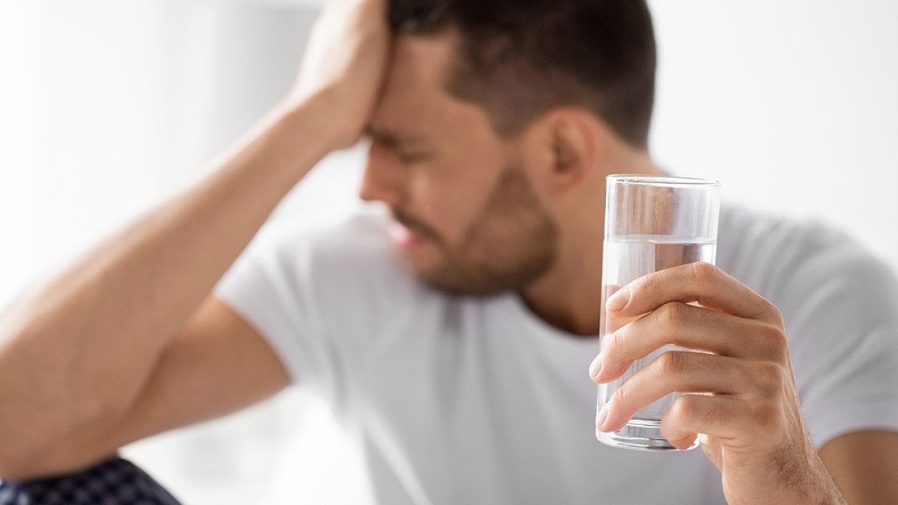 Man experiencing hangover holding a glass of water.