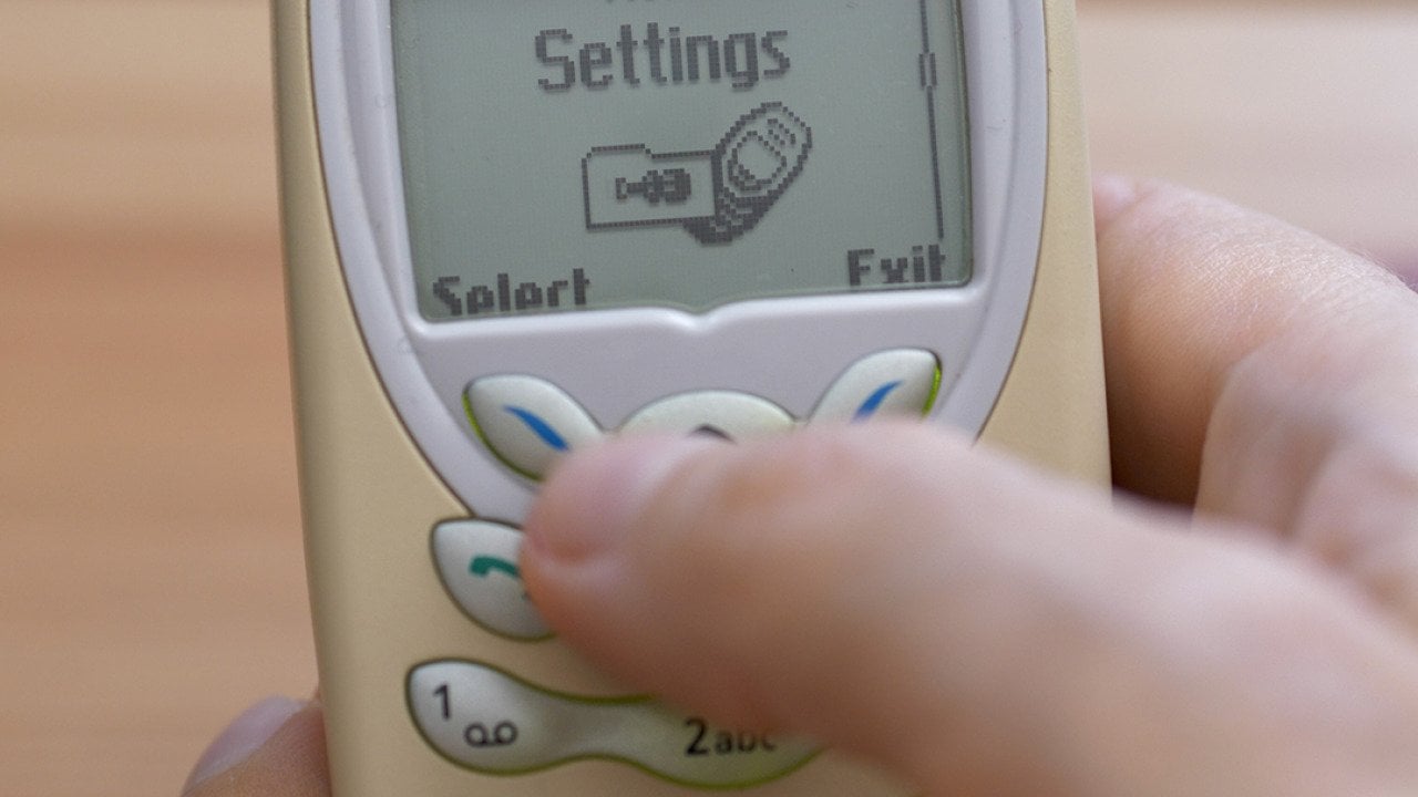 A retro Nokia 3410 mobile phone in someone's hand with the settings menu open.