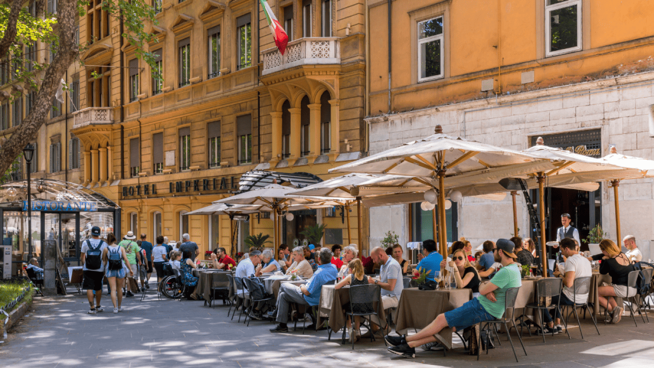Tables under umbrellas filled with people outside of restaurants in Rome. 