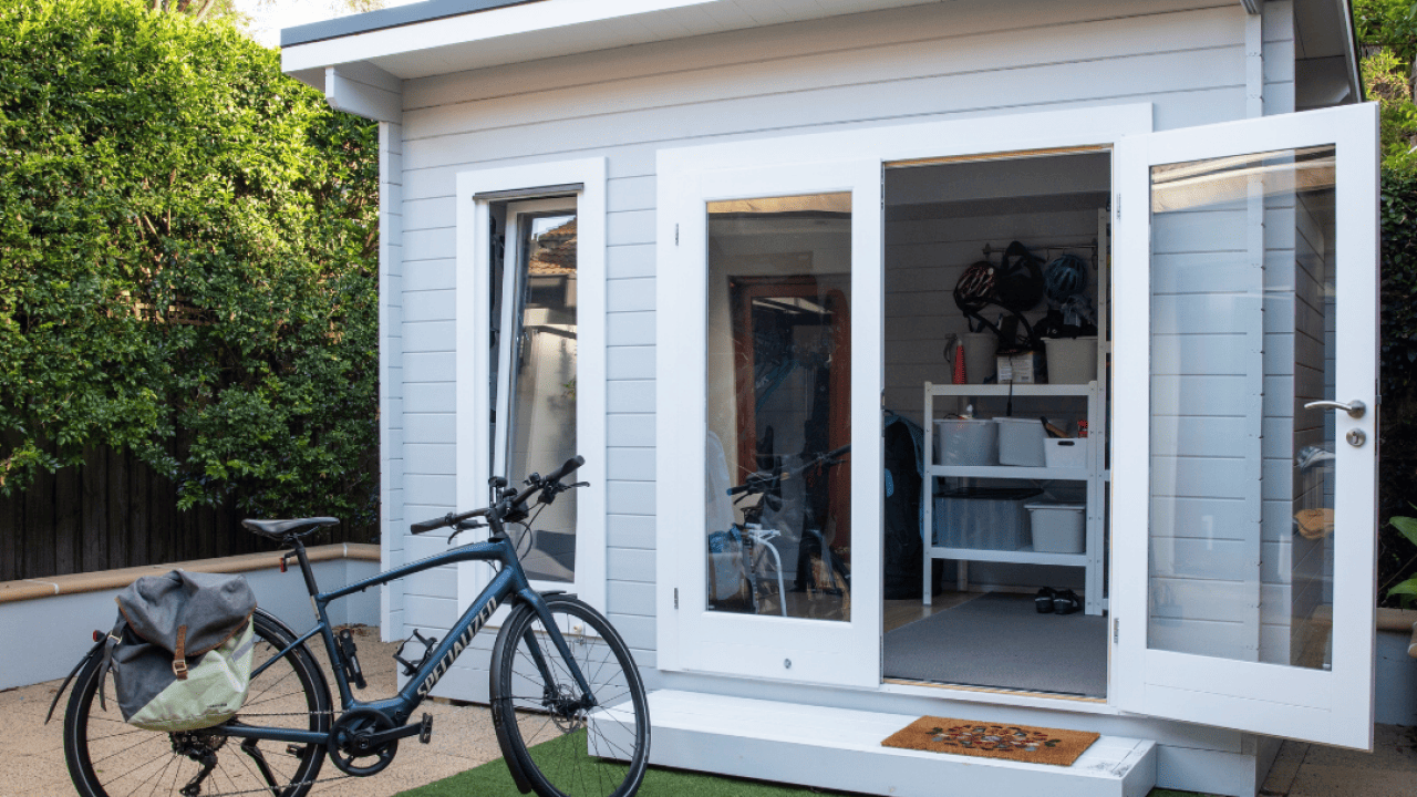 A nice shed with the doors open and a bike parked in front of it. 