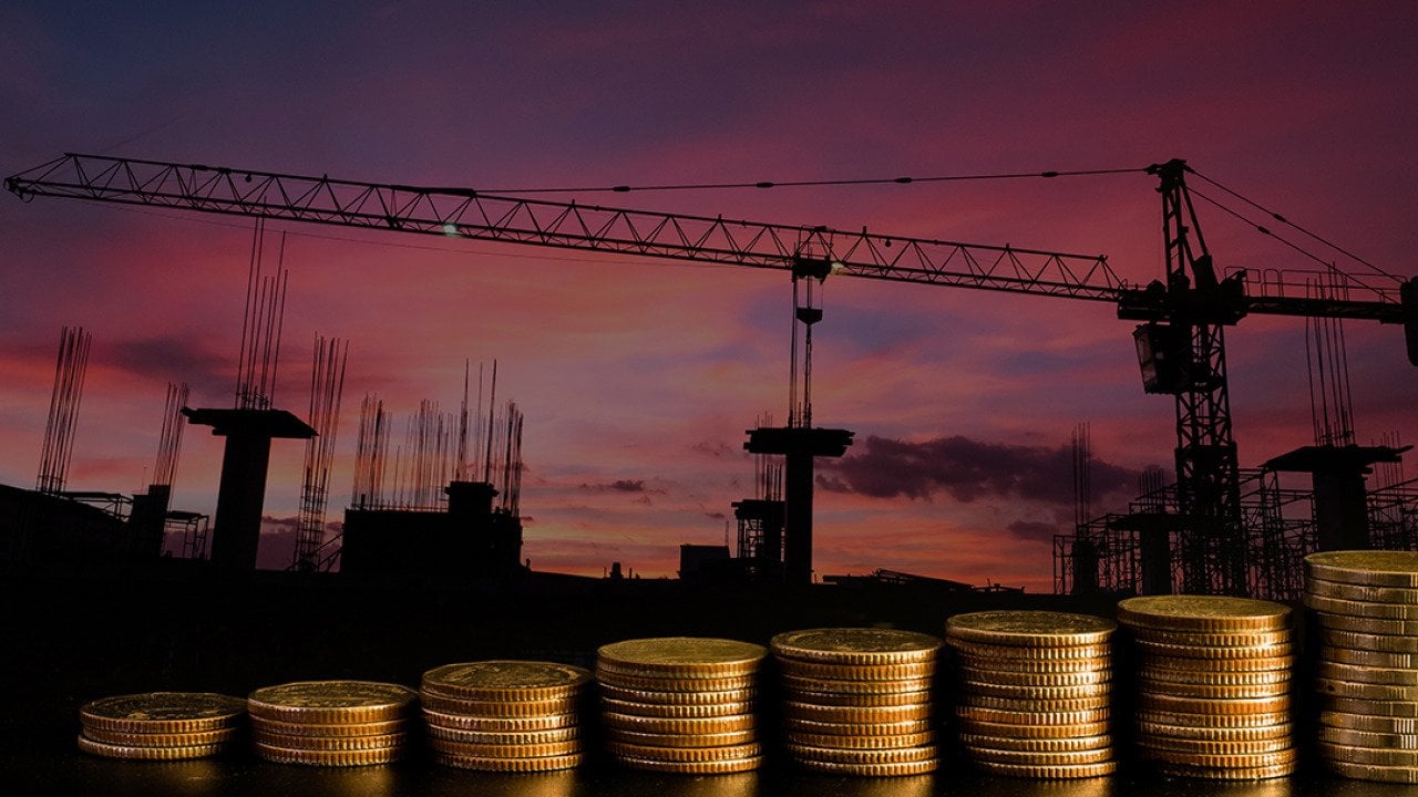 A row of stacked coins with an estate construction site background.