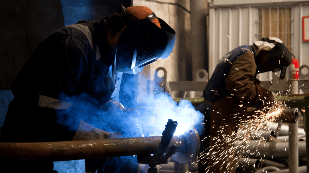 Two welders with protective masks welding metal, with sparks flying around.