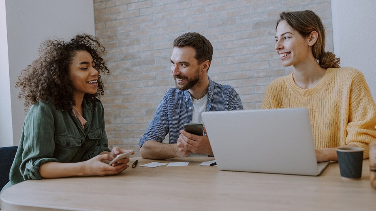 A 3-member creative team engaged together in a discussion in an office.