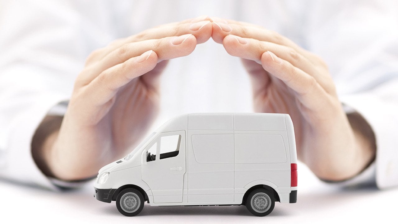 A figure of a small transport van protected by hands of a car insurance agent.