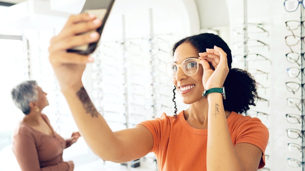 A young woman trying on eyeglasses in a shop and taking a selfie.