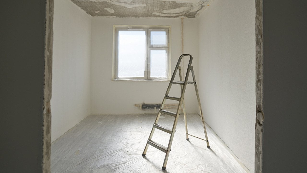 A ladder at the center of an apartment room with unfinished interior paint. 