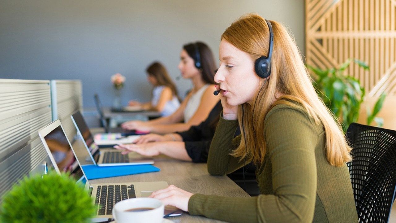 A row of female customer service representatives taking calls in their office.