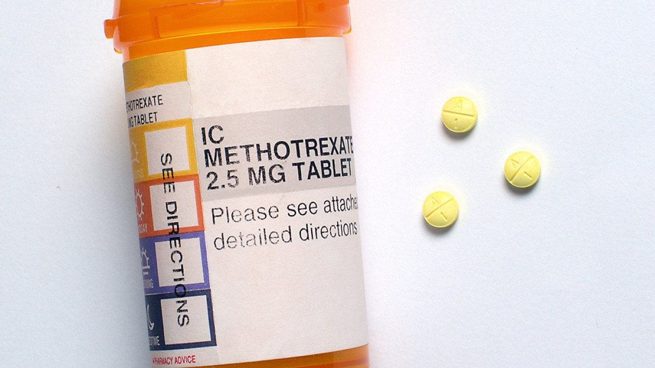 Three generic Methotrexate pills beside a prescription bottle.
