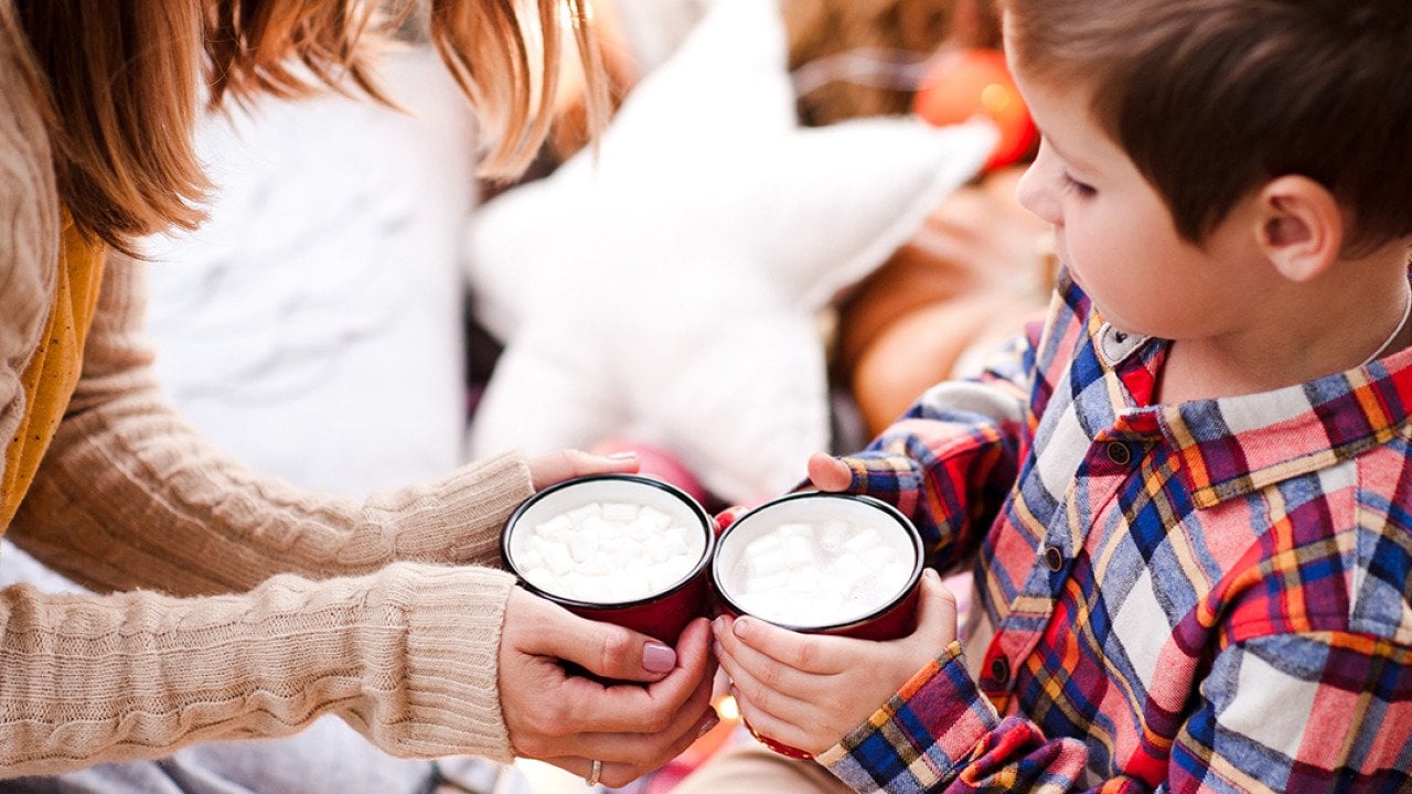 A young boy holding a cup of hot chocolate with his mother.