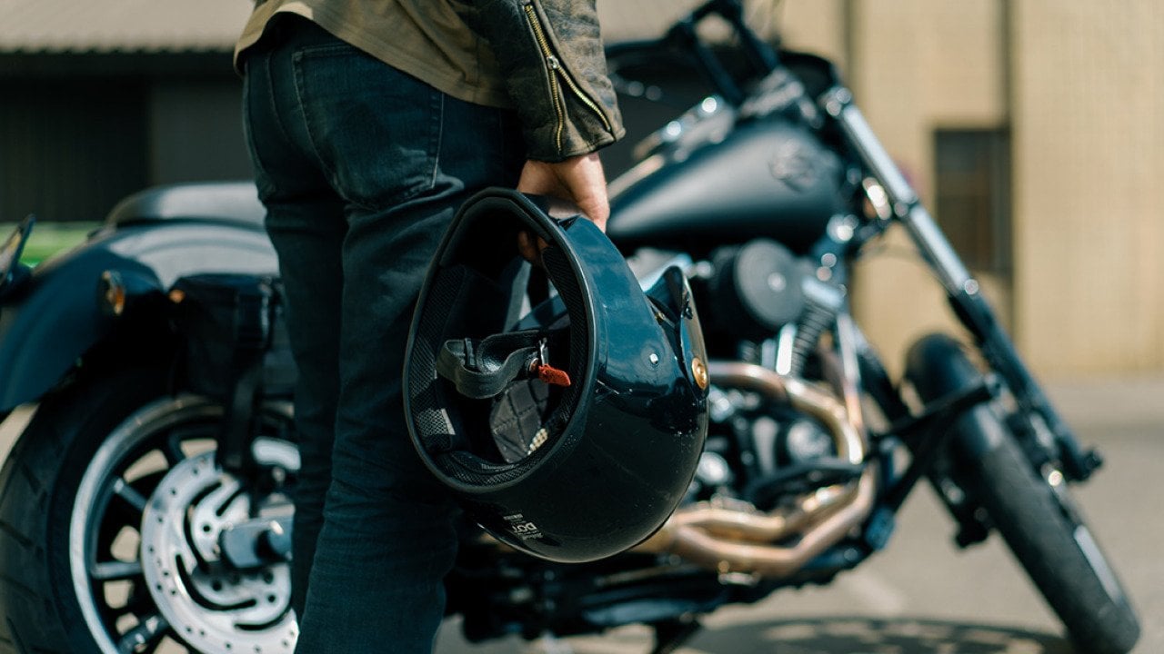 Close up of person holding motorcycle helmet with Harley type motorcycle in the background.