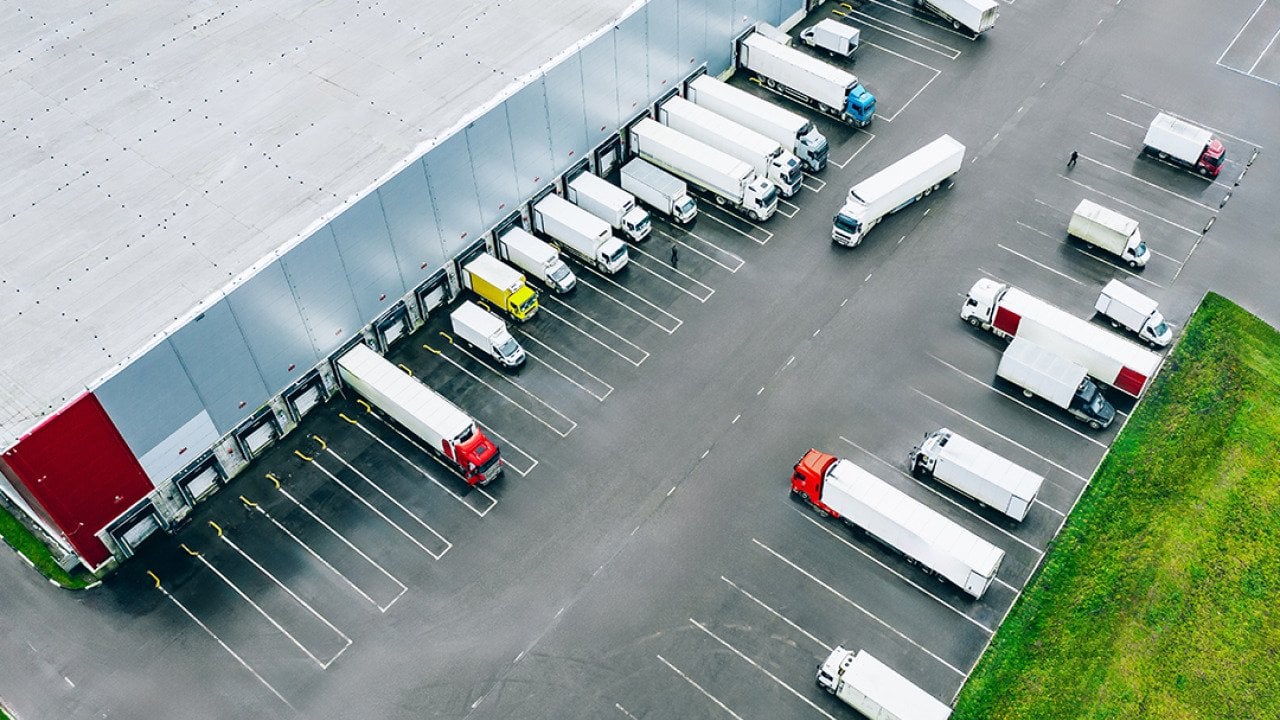 Aerial view of logistic trucks lined up at the loading docks of a large distribution warehouse.