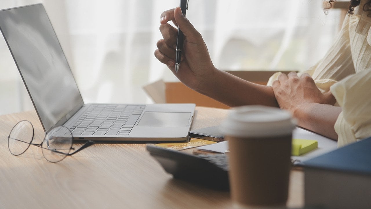 A female entrepreneur holding a pen while working with a laptop.