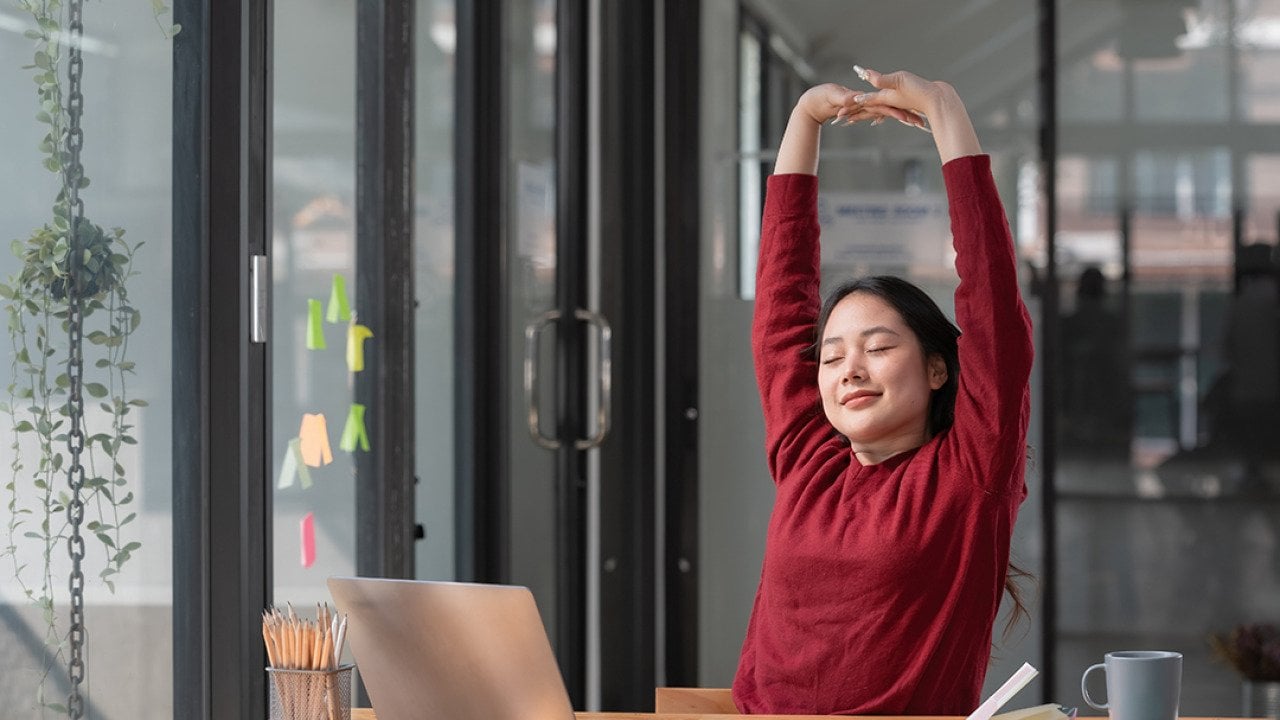 A young female employee stretching up her hands while working in the office.