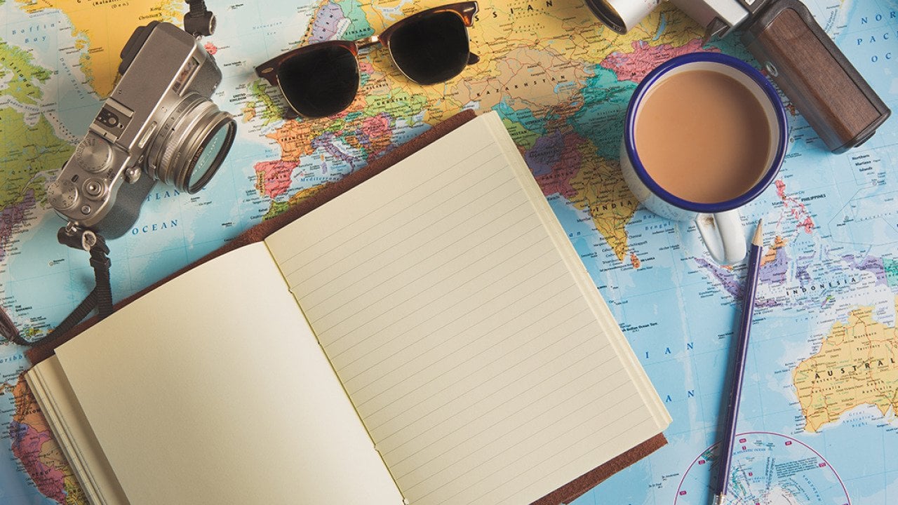 Traveller items such as a camera, sunglasses, and an empty planner on top of a world map.