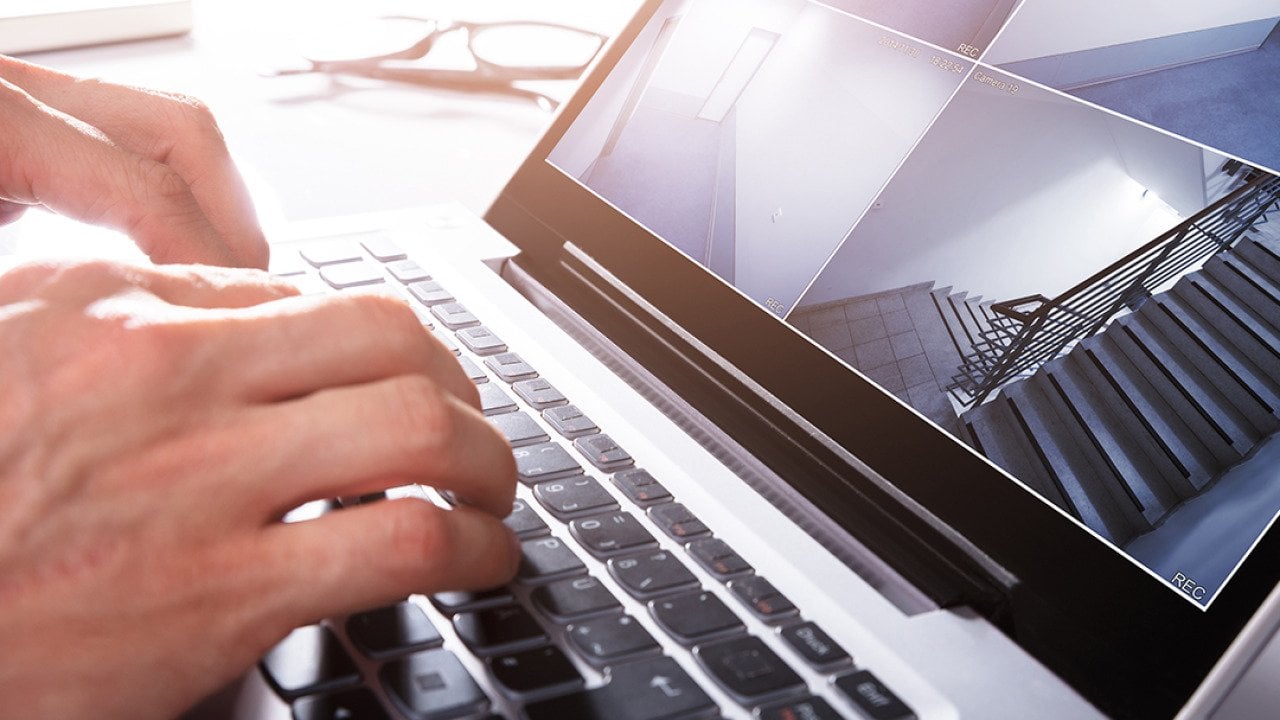 Person monitors a split screen view of CCTV footage using a laptop.