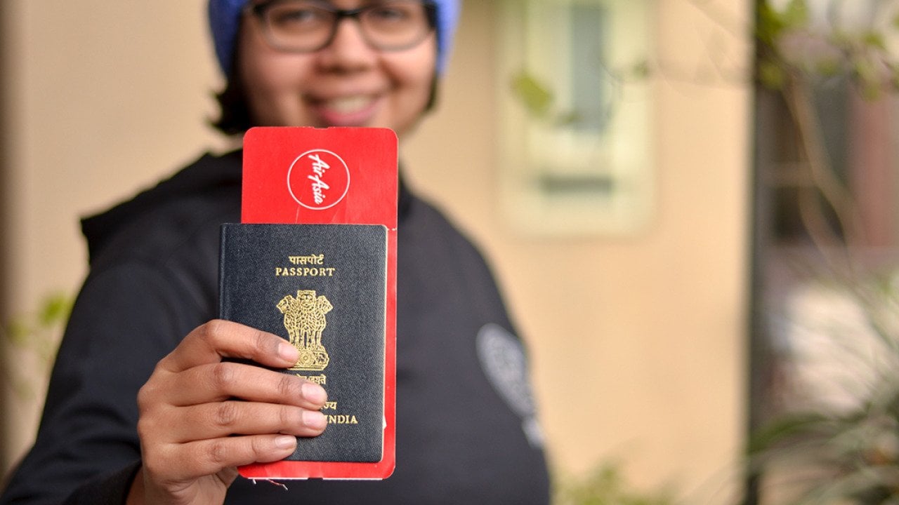 Portrait of a young Indian woman holding up her passport with an international flight ticket.
