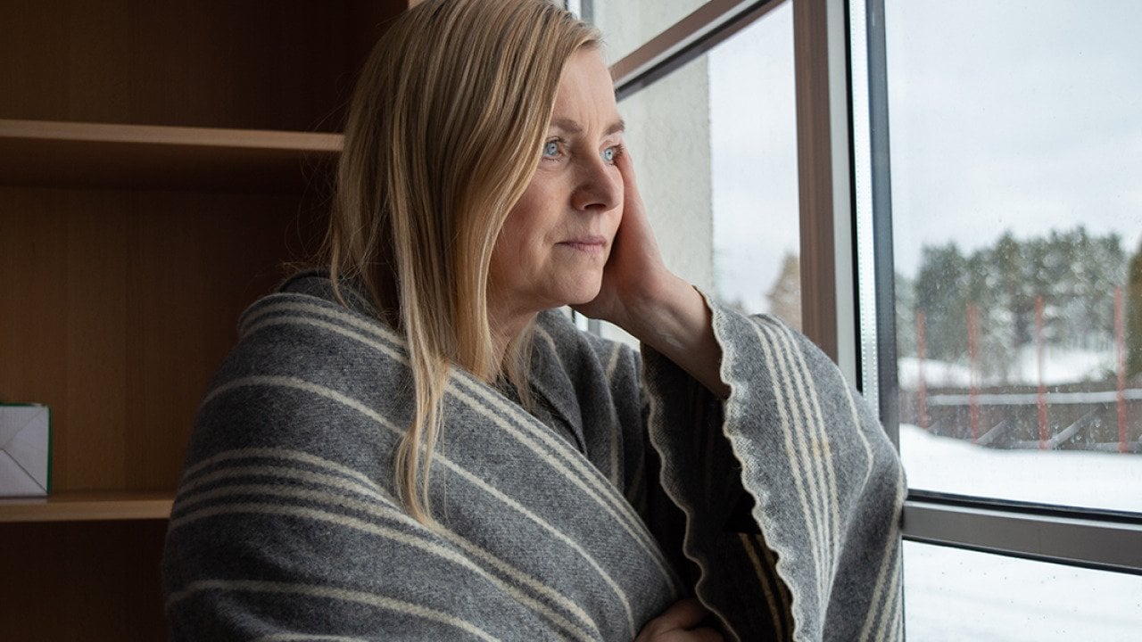Woman wrapped in blanket looking out the window during winter.